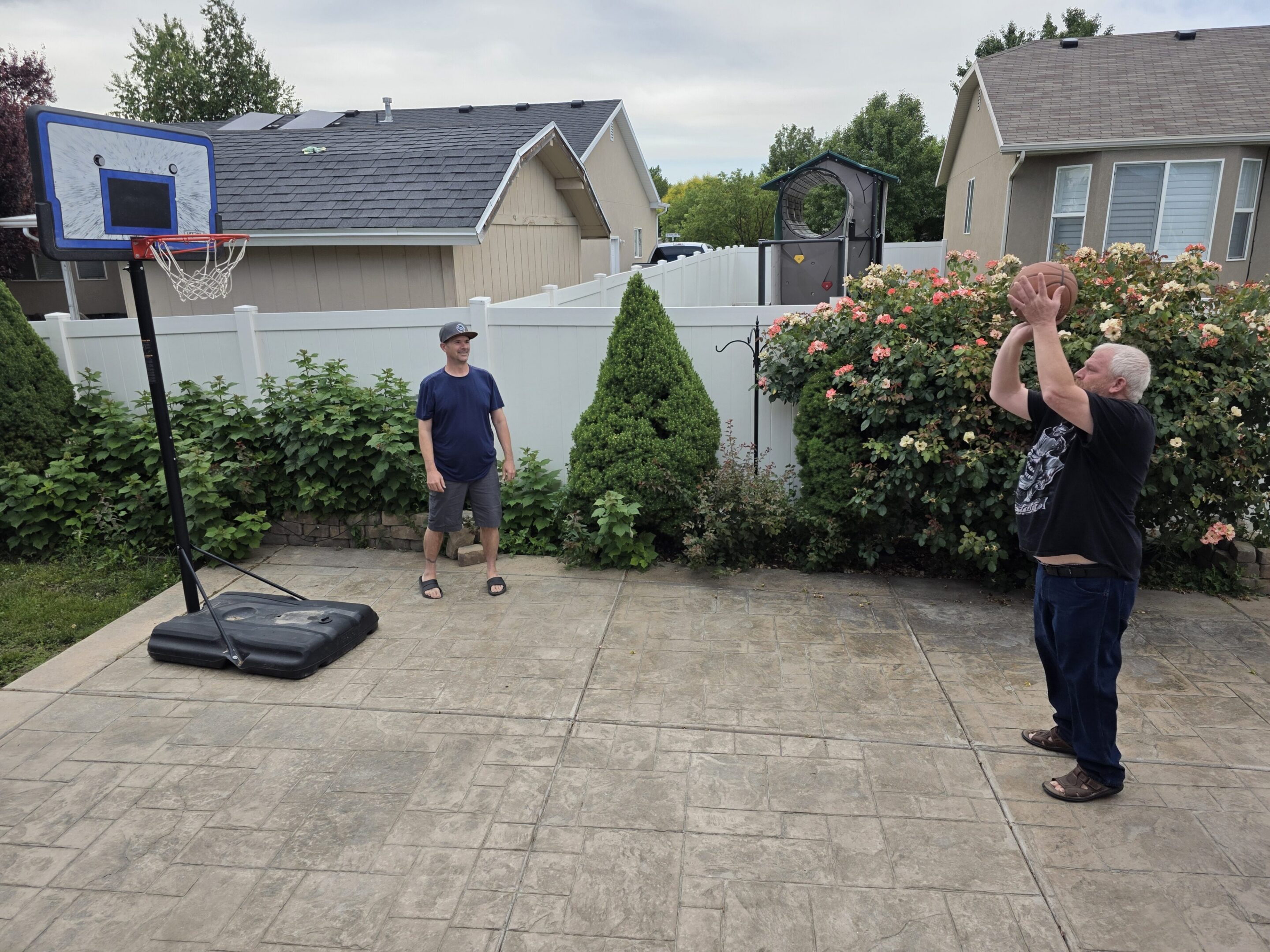Two people playing basketball on backyard patio