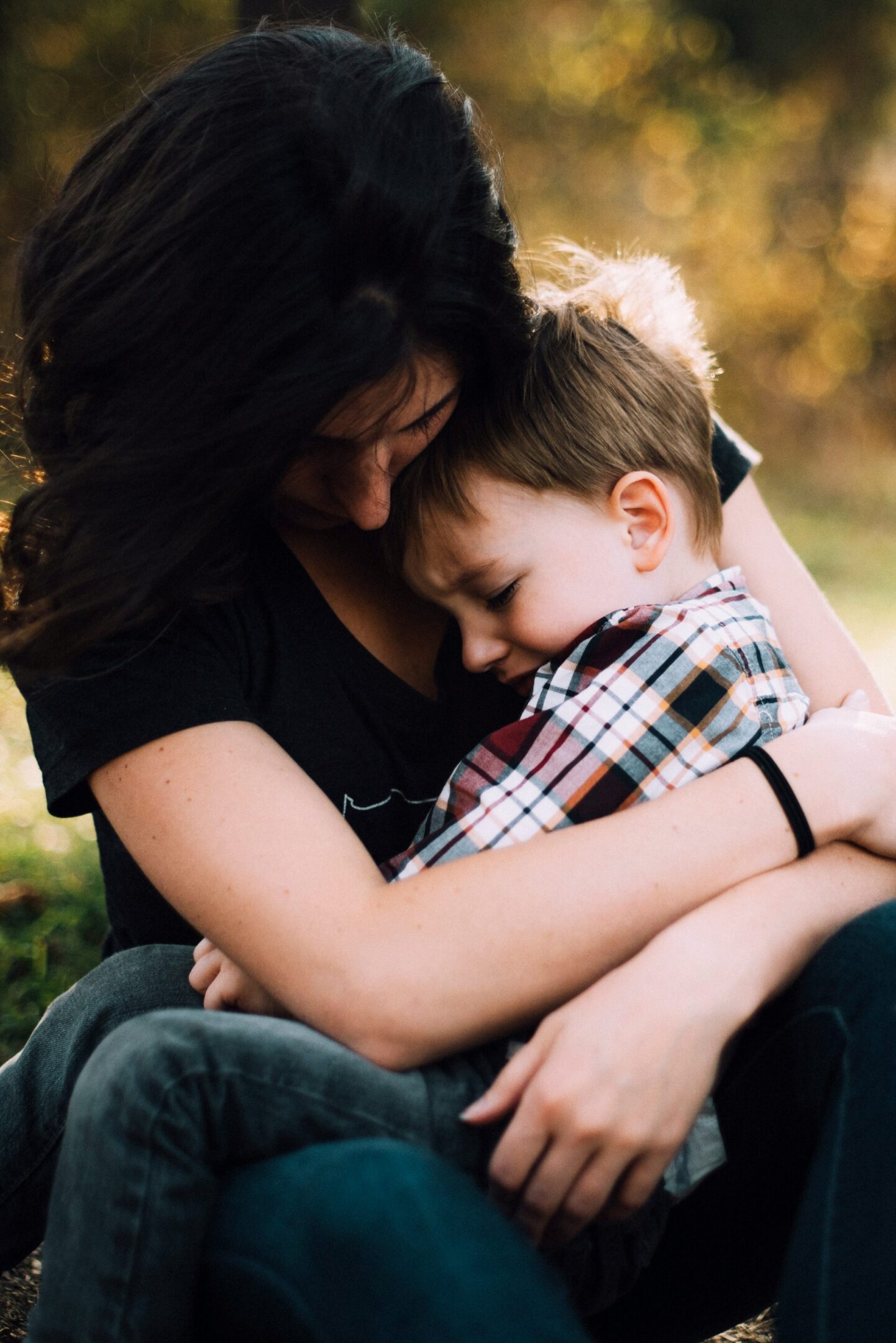 Woman embracing young boy outdoors in sunlight