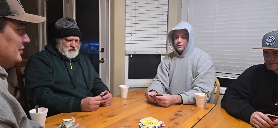 Four men playing cards around wooden table